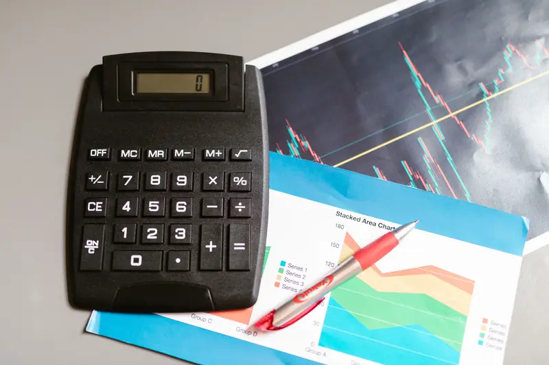 Desk calculator resting on printed stock and area charts with a red pen