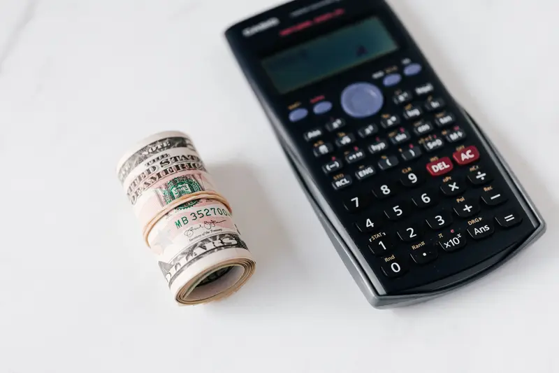 Roll of US dollar bills held with a rubber band next to a scientific calculator