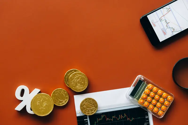 Gold coins and a percent sign beside a printed stock chart and pocket calculator