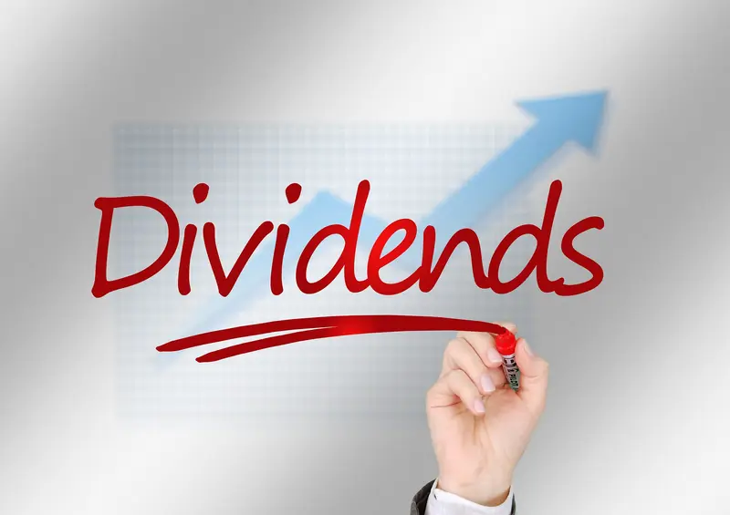Hand writing the word Dividends in red marker over a rising chart arrow