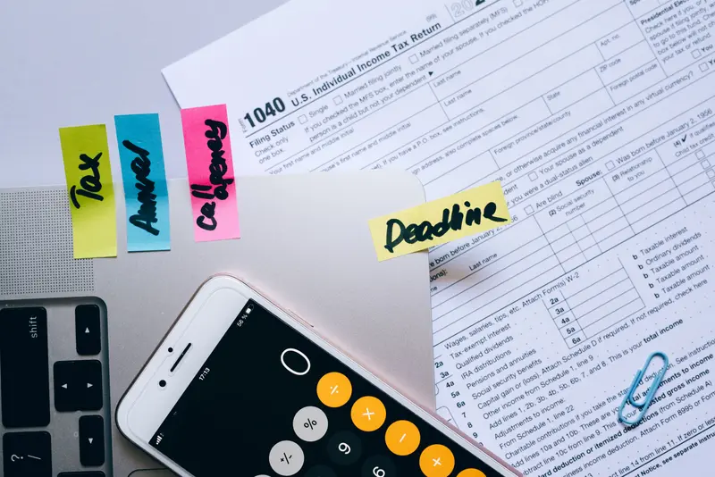 IRS Form 1040 with sticky notes reading Tax, Annual and Deadline beside a phone calculator